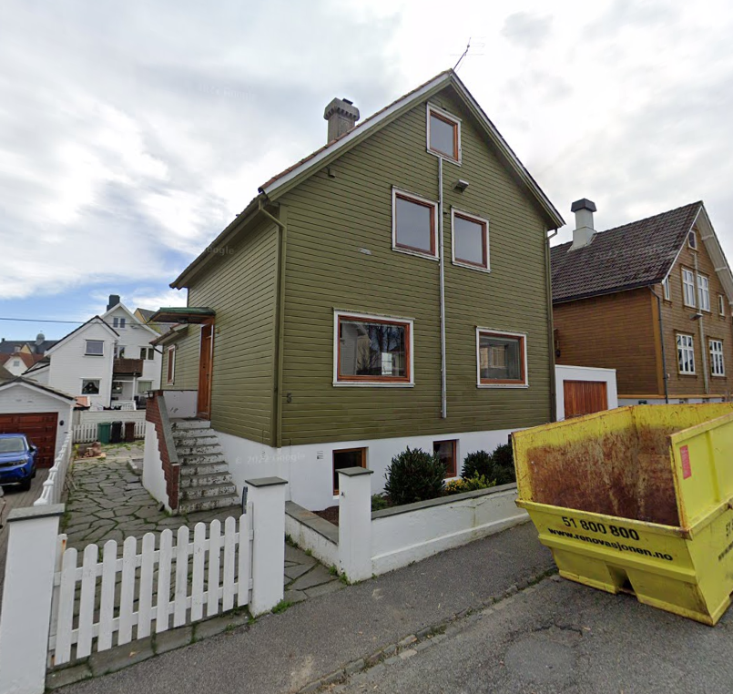 Hus med husmorvinduer og hellelagt gårdsrom, og tom konteiner utenfor.