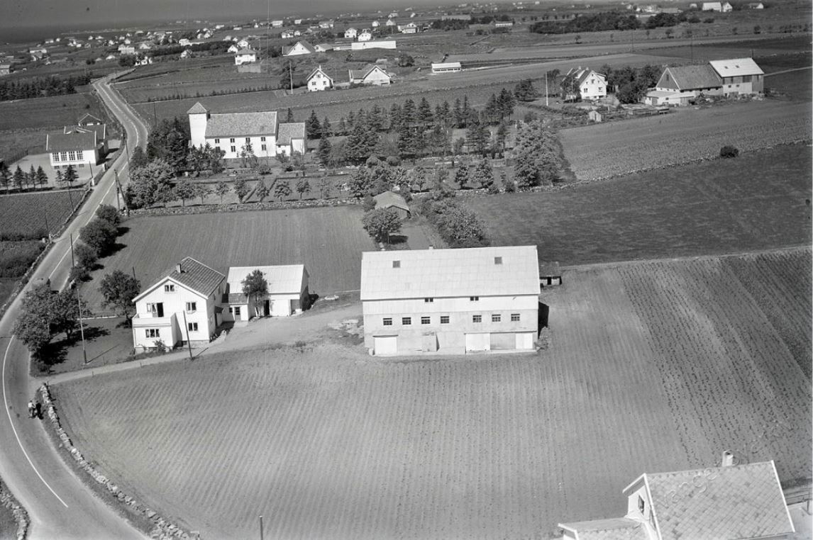 Et gammelt flyfoto over Revheim. Jordbruksmarker og spredt bebyggelse, steingarder og trerekker.