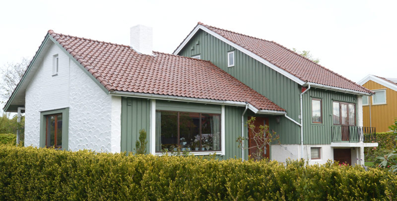 Grønt hus med hvit murvegg på gavlen. 