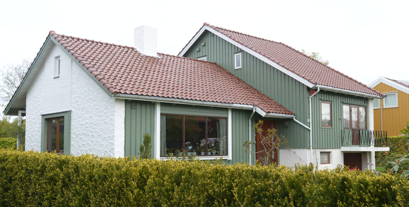 Grønt hus med hvit murvegg på gavlen.