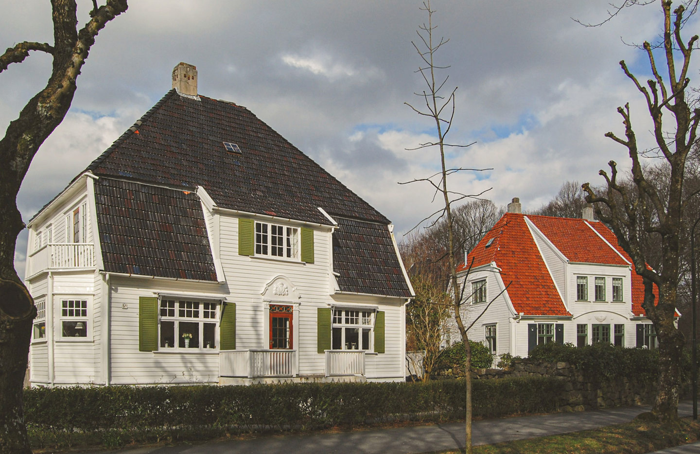 Stort, flott jugendhus med store takplater. Hvit kledning og grønne skodder.