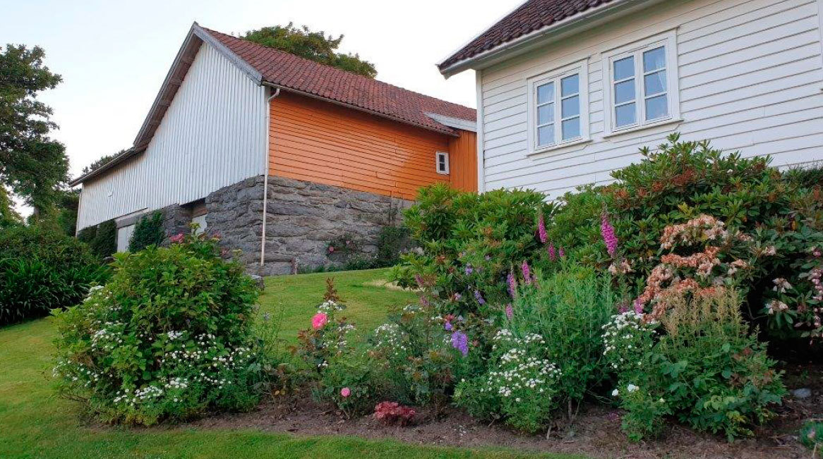 Hage på Bru, med gårdsbygning i bakgrunnen.