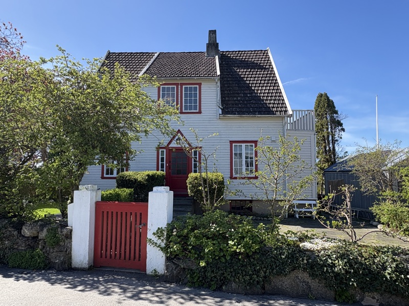 Husets fasade og forhage med rød port.