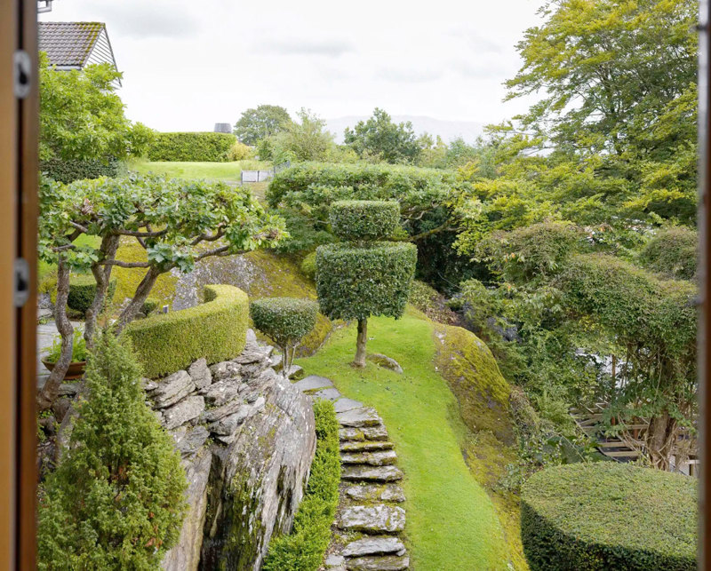 Utsikt over frodig hage med skulpturelle trær. 