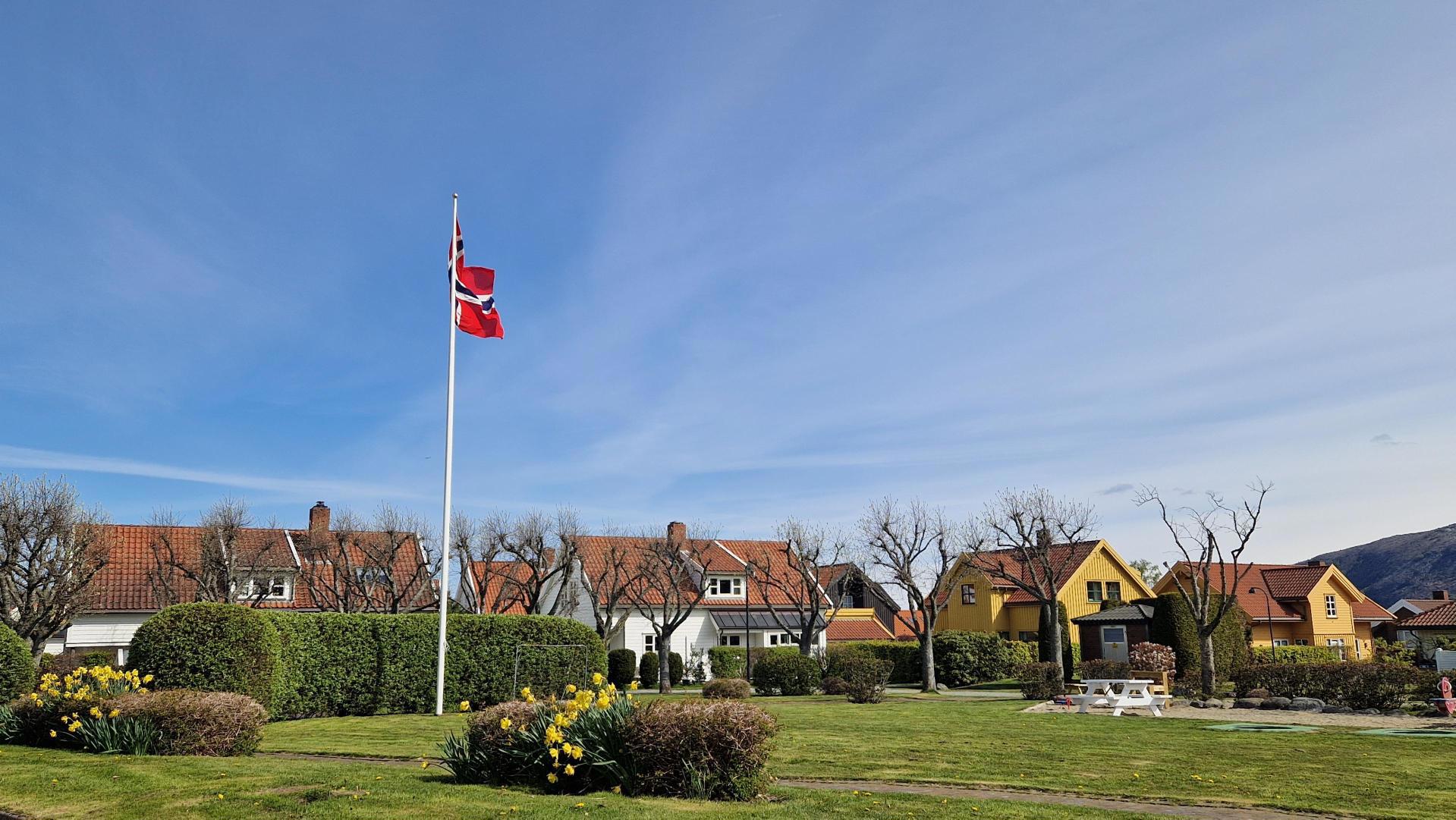Stor gressplen med flaggstang, fotballmål og nedfelte trampoliner.