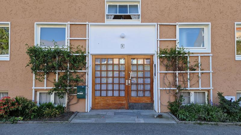 Inngangsparti med teak-dør med et nett av smårutete vinduer. Klatreplanter vokser opp langs espalier på hver side. 