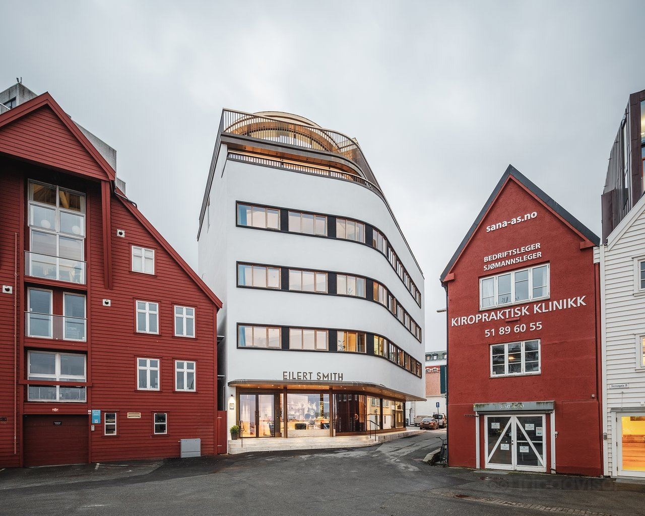 Funksjonalistisk hotellbygg med smekre linjer, mellom to røde sjøhus.