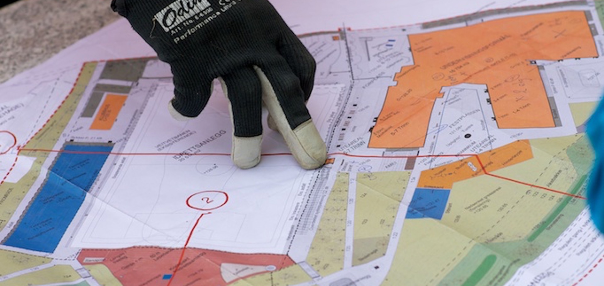 Hansker som peker på arkitekttegninger på en byggeplass.