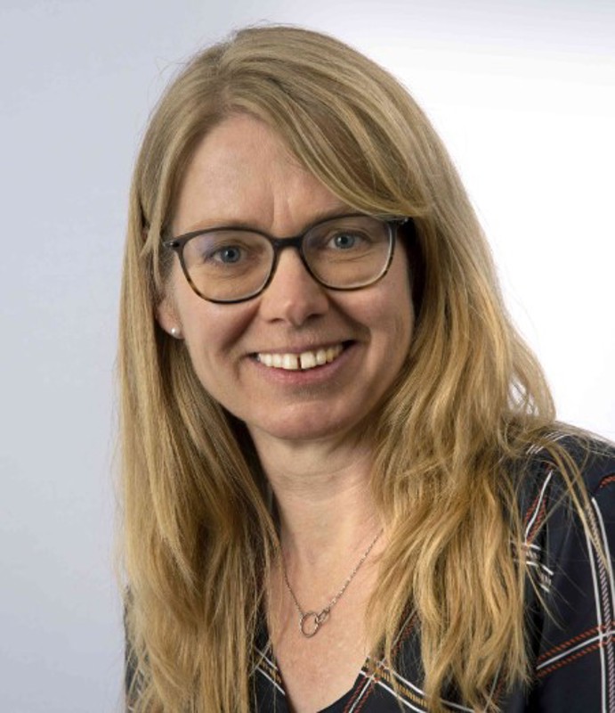 ansikt av smilende kvinne med langt mellomblondt hår og briller.