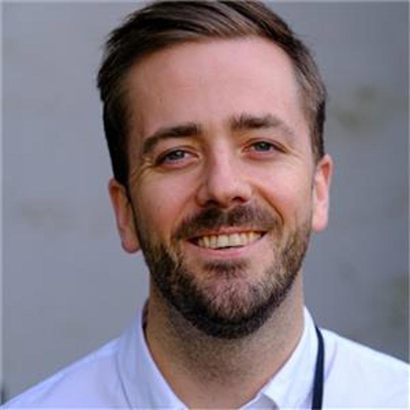 Ansiktet til smilende mann med kort mørkt hår, skjegg og bart.