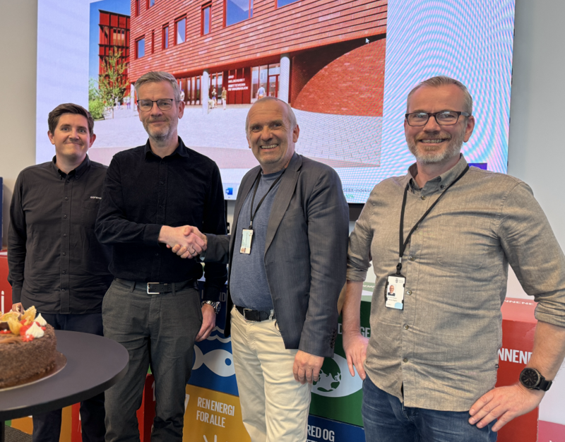 Fire herrer smiler til kamera etter kontraktinngåelsen. Det skimtes en kake.