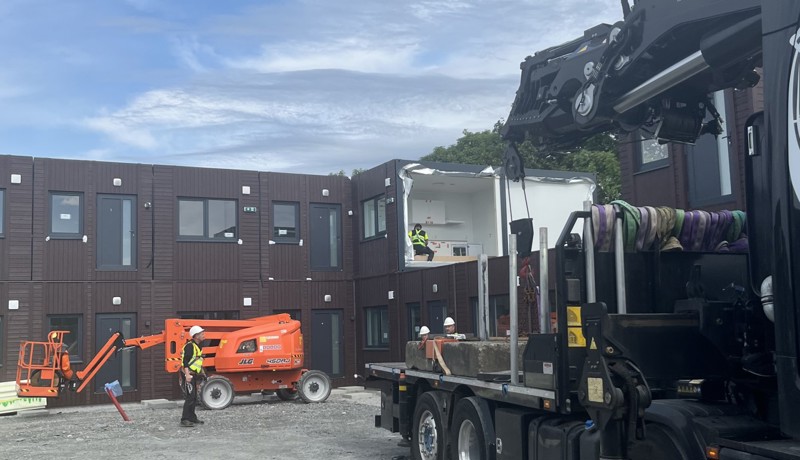 Moduler til boliger heises settes sammen i to etasjer. I forgrunnen en kranbil.