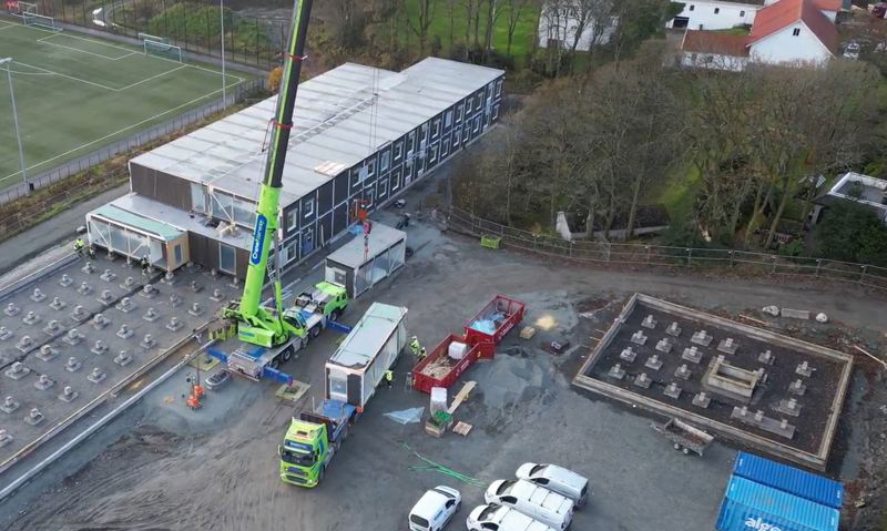 Kranbil løfter moduler til skolebygg på plass. Flere moduler er satt opp og bygget tar form.