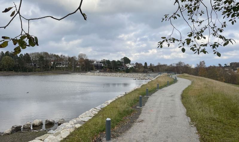 Tursti oppå bred demning, til venstre et tjern