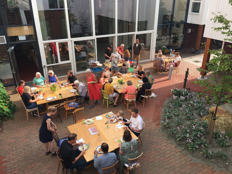 Folk som sitter og spiser rundt flere bord i gårdsrom. Foto: Siv H. Stangeland