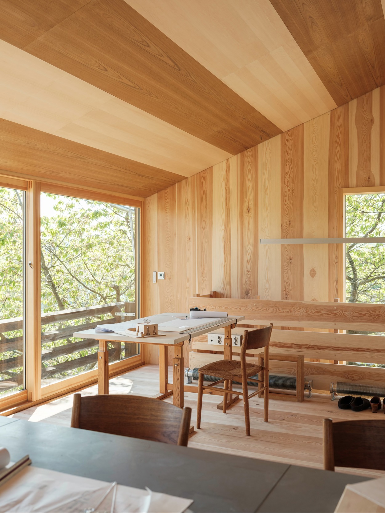 Interiør der taket er kledd med finer i vekselsvis mørkt og lyst treslag. Arkitektpult midt på bildet.