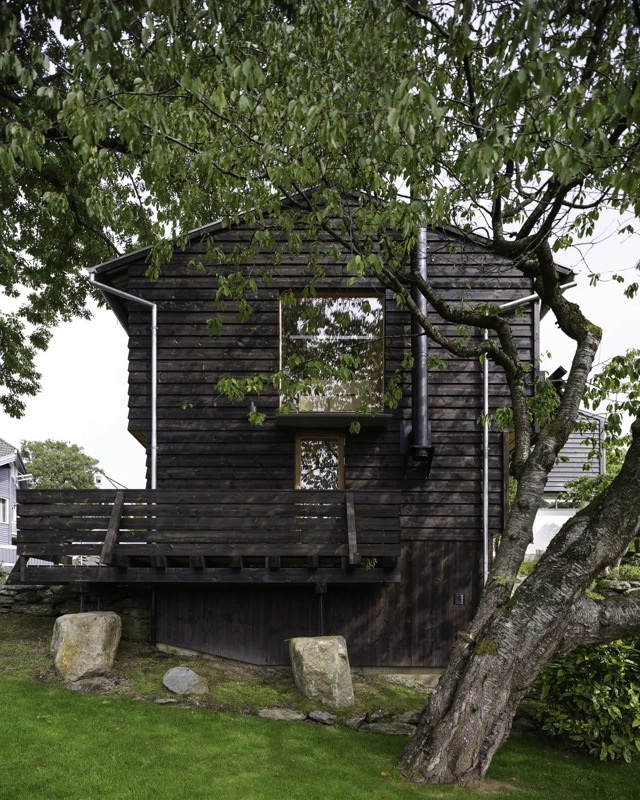 Et lite hus med nesten stabbur-aktig form, og med et tre redd ved siden av.