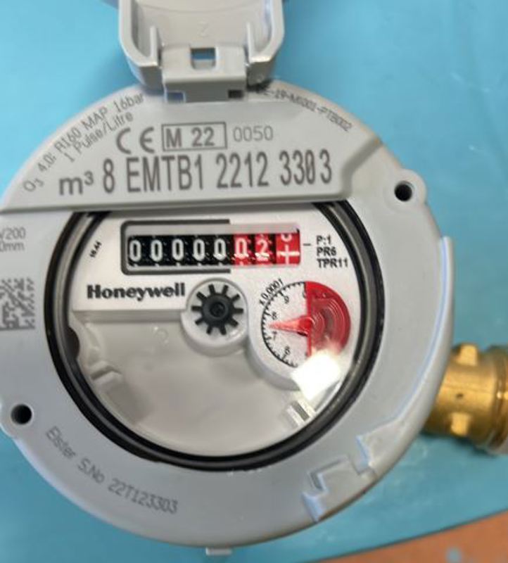 Vannmåler med telleverk bak en rund glassplate. De tre bakerste tallene i telleverket, bak et komma, er røde.