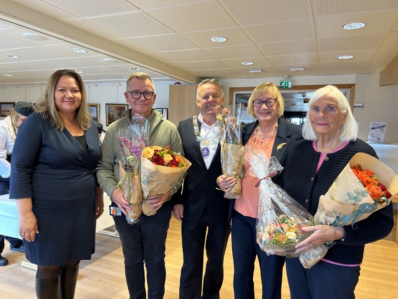 Fire personer står ved siden av hverandre inne på Øyane sykehjem med smilende fjes og blomster i armene.