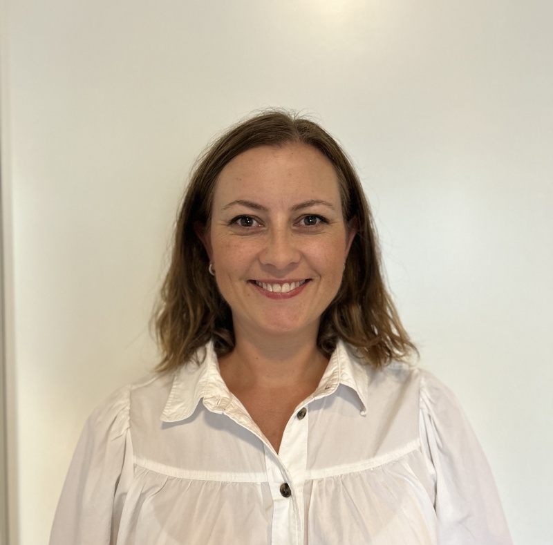 Ansiktsbilde av Marie Therese. Hun har brune øyne, et stort smil, hvit skjorte og langt, brunt hår med midtskill.