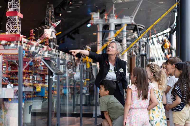 Voksen kvinne som viser noe til barn på museum. 