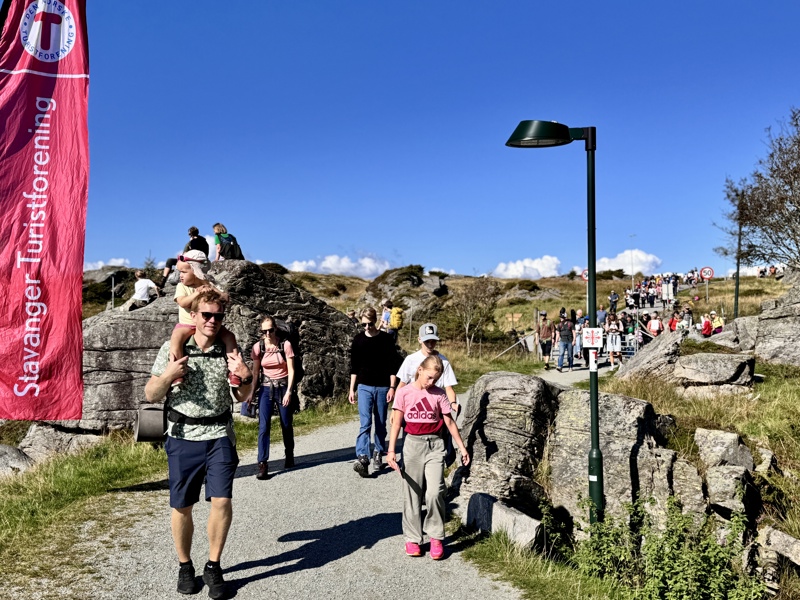 En voksen mann har en liten jente på skuldene. Resten av familien følger i bakgrunnen. 