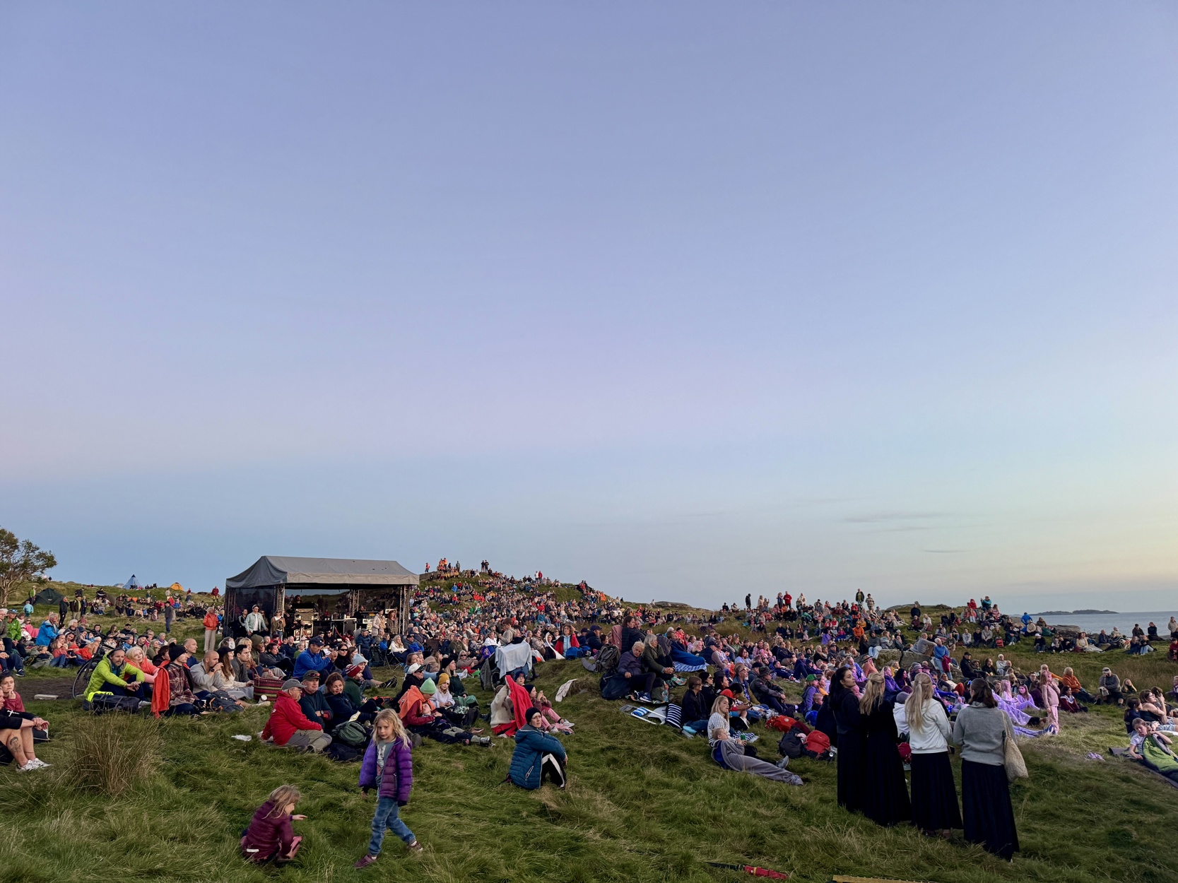 Et folkehav av mennesker sitter på jakker og liggeunderlag.