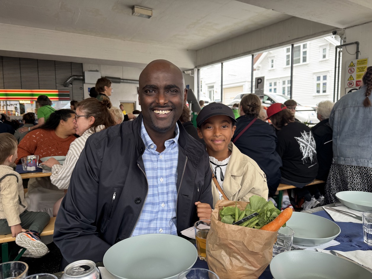 En voksen mann og hans datter smiler til kamera, de sitter på langbord.