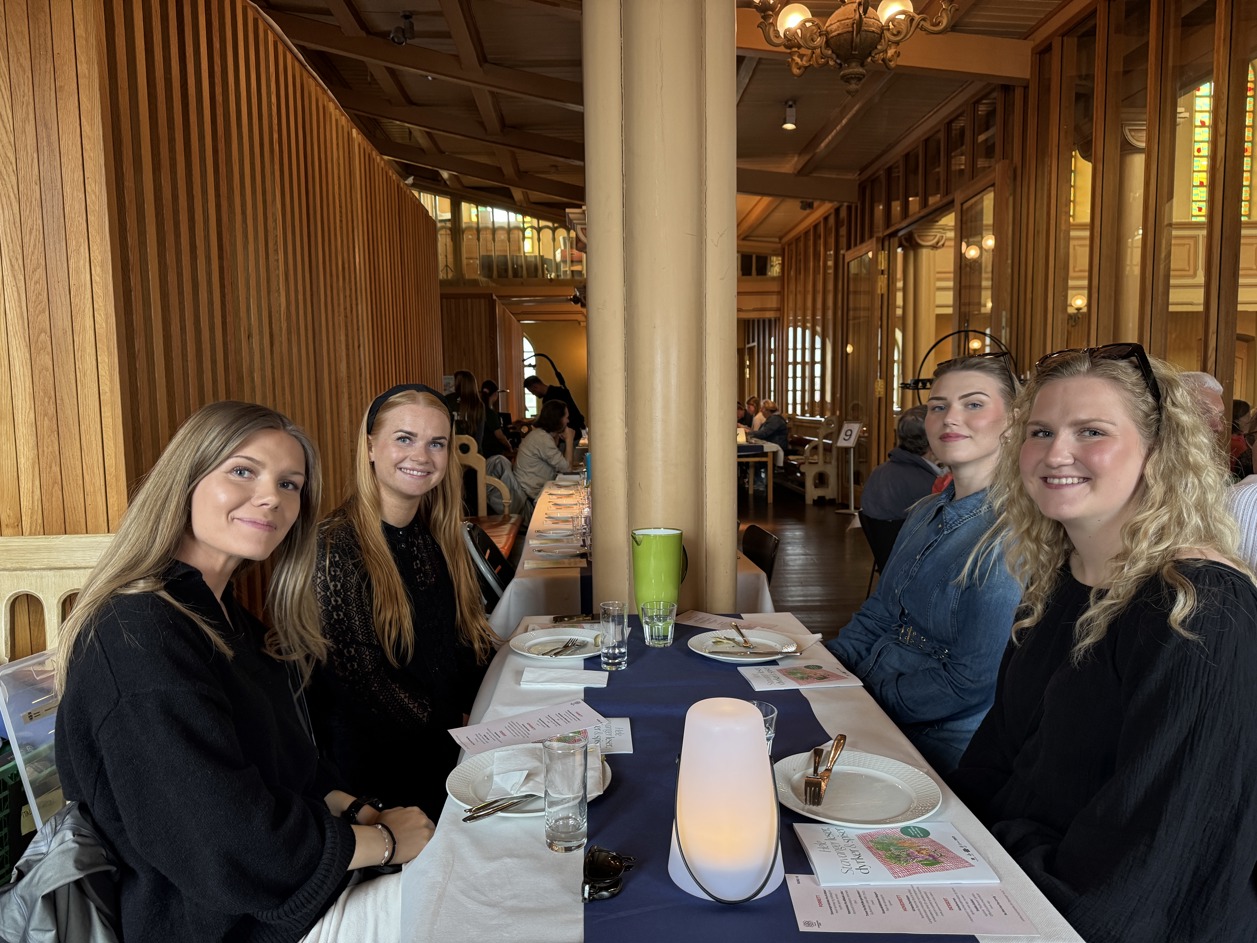 Fire unge jenter smiler til kamera. De sitter på langbord i Petrikirken.