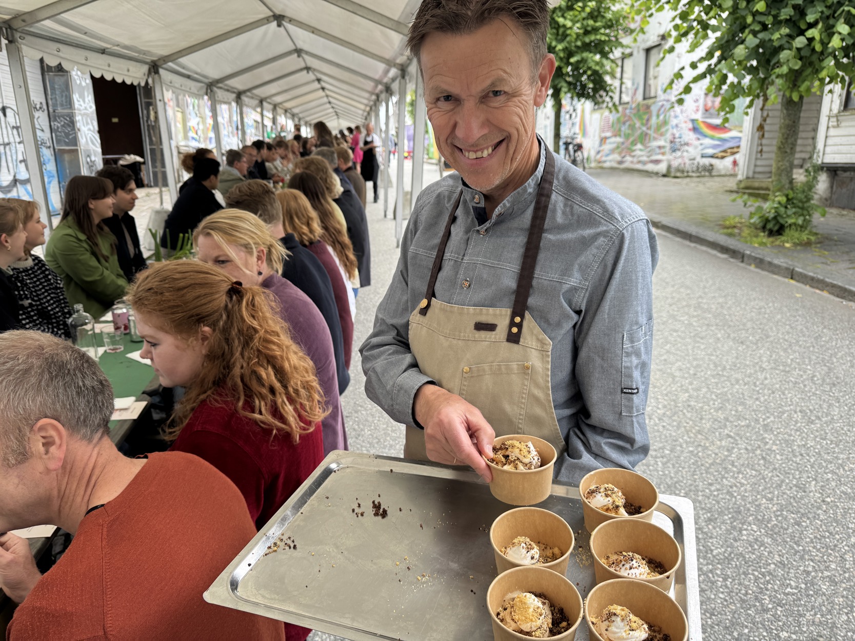 Voksen mann smiler til kamera mens han deler ut deilig isdessert.