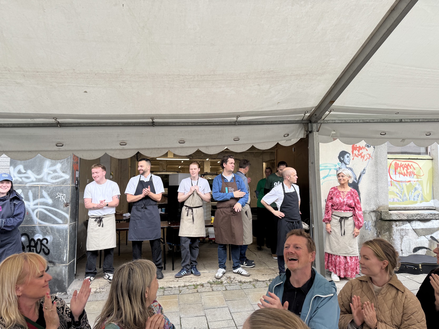 Kokkene smiler i bakgårdsåpningen. Gjestene fra langbordet smiler og applauderer.