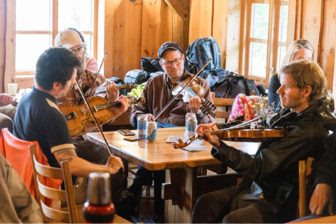 Fire menn spiller fele rundt et bord innendørs.