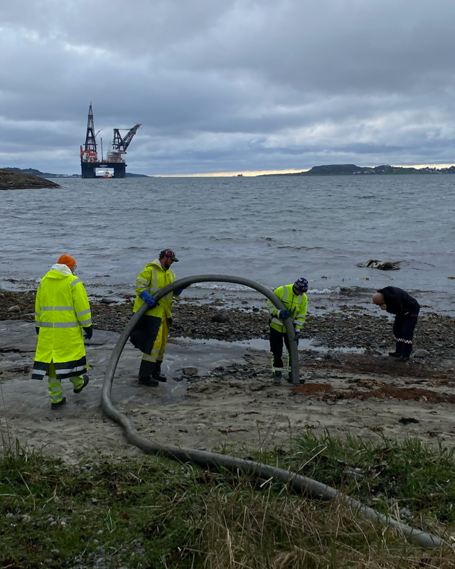 arbeidsfolk med sugeslange. kranbåten sleipnir i bakgrunnen