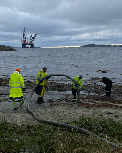 arbeidsfolk med sugeslange. kranbåten sleipnir i bakgrunnen
