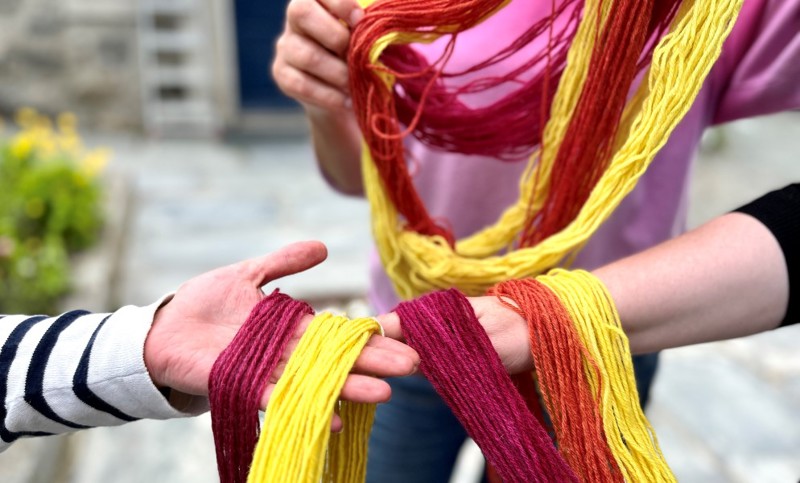 Vi ser hendene til tre personer som holder naturfarget garn i hendene. 