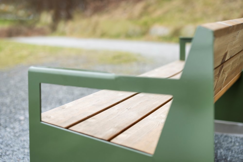 Bildet viser benken, et nærbilde hvor vi ser den grønne stålrammen og treplankene som er i setet.
