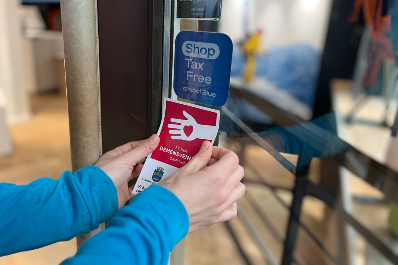 To hender som plasserer demensvennlig klistremerket på en inngangsdør.