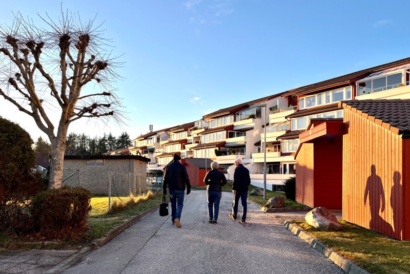 Vi ser Mjughaug terrasse fra forsiden, med gangveien hvor vi ser tre av naboene som går på veien. 