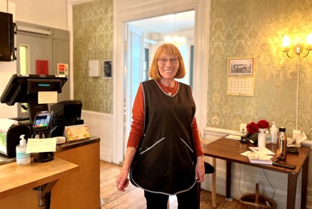 Vi ser Inger Paulsen som står blid og fornøyd i forkle foran disken.