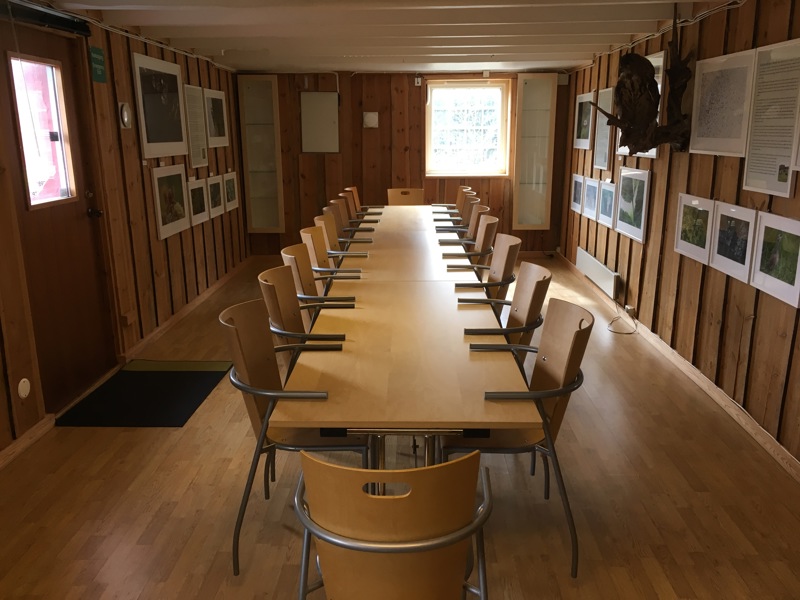 Viser et bilde av bord og stoler i et rom. Det henger naturfotografier på veggene.