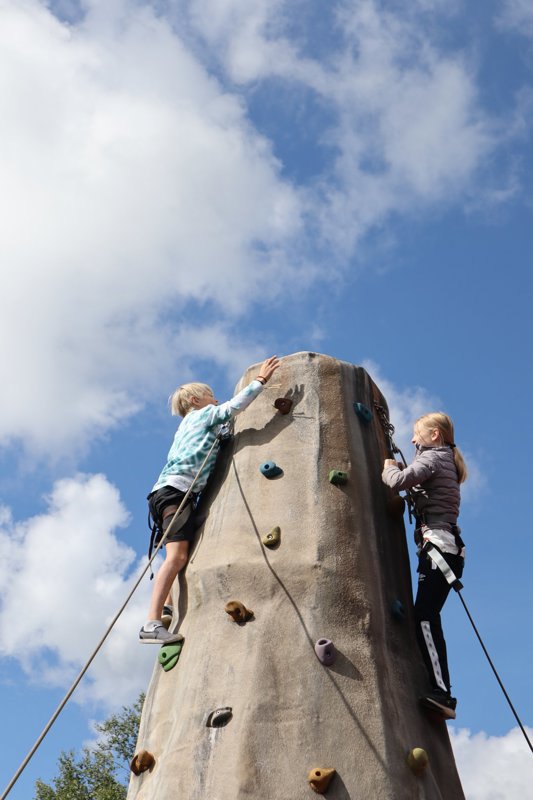 To barn med klatreutstyr klatrer opp en klatresøyle.