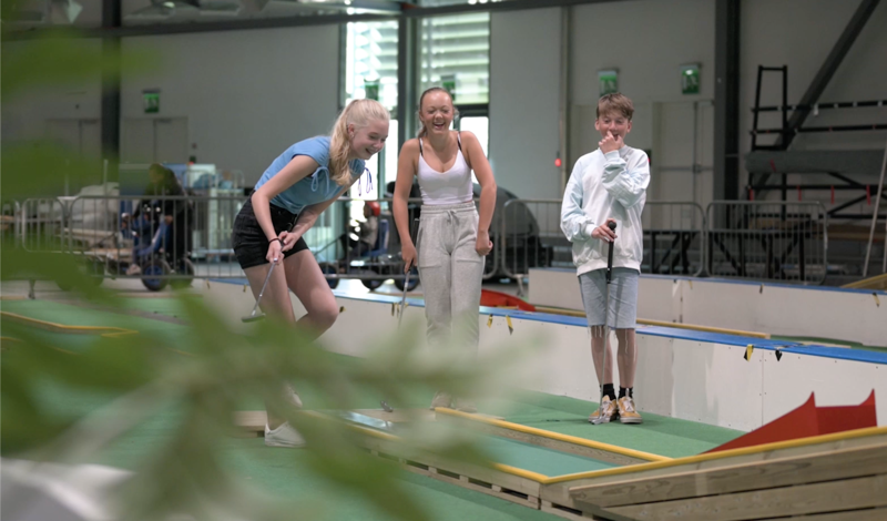 Tre ungdommer ler mens de spiller minigolf inne i Sørmarka arena.