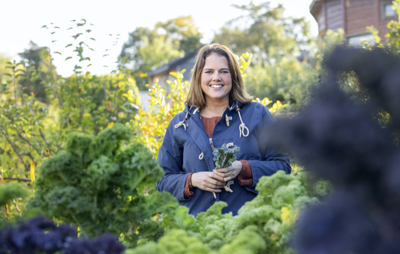En smilende dame blant planter i kolonihage
