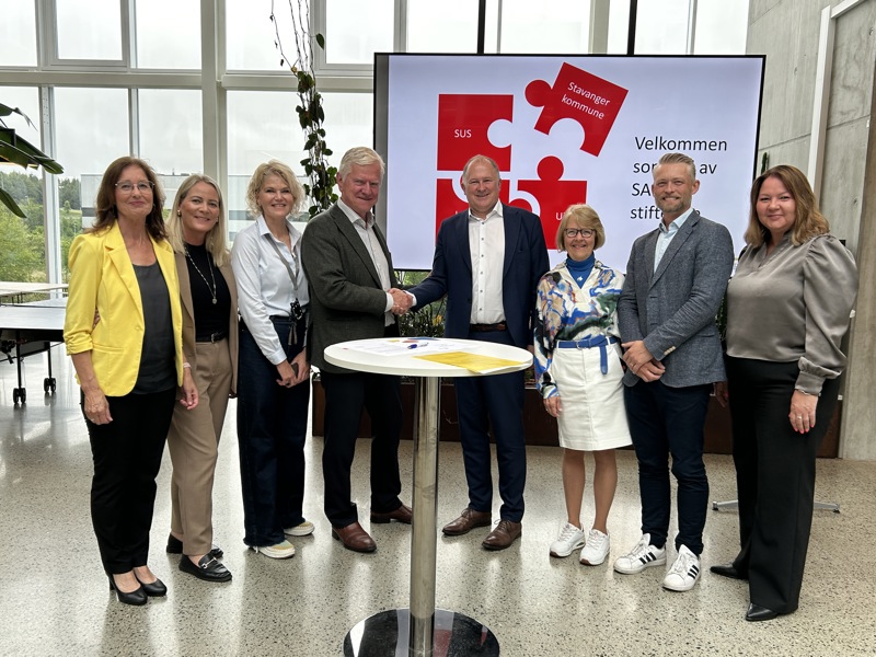 Åtte representanter for UiS, SUS, Stavanger kommune og SAFER står skulder ved skulder bak et rundt bord der avtalen ble signert.