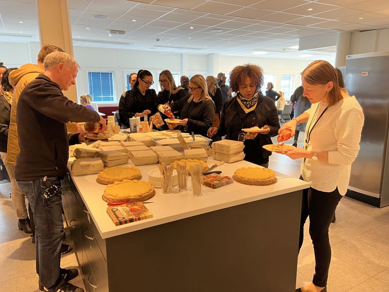 En gruppe mennesker forsyner seg med mat og kaker rundt en kjøkkenøy.