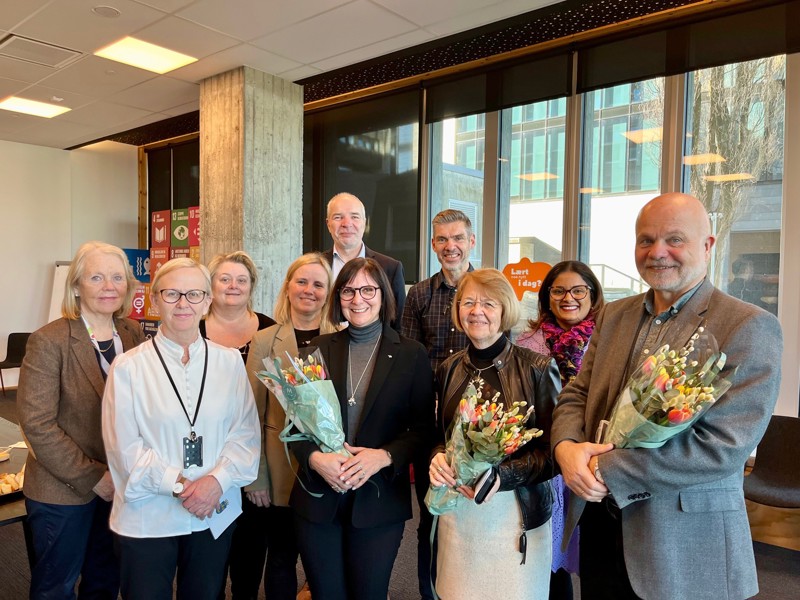 Bildet viser ni personer, hvor to holder blomsterkvaster i hendene.