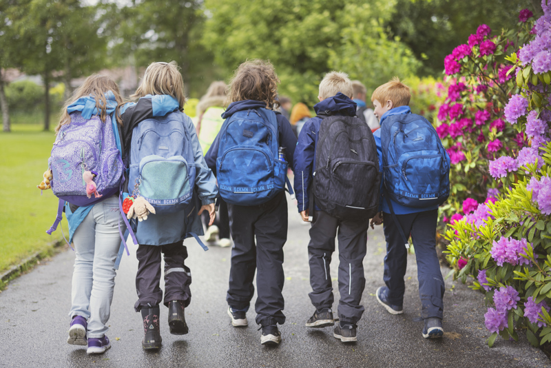 Bildet viser en gruppe skolebarn på tur. Bildet er tatt bakfra, barna har skolesekker og turtøy på.