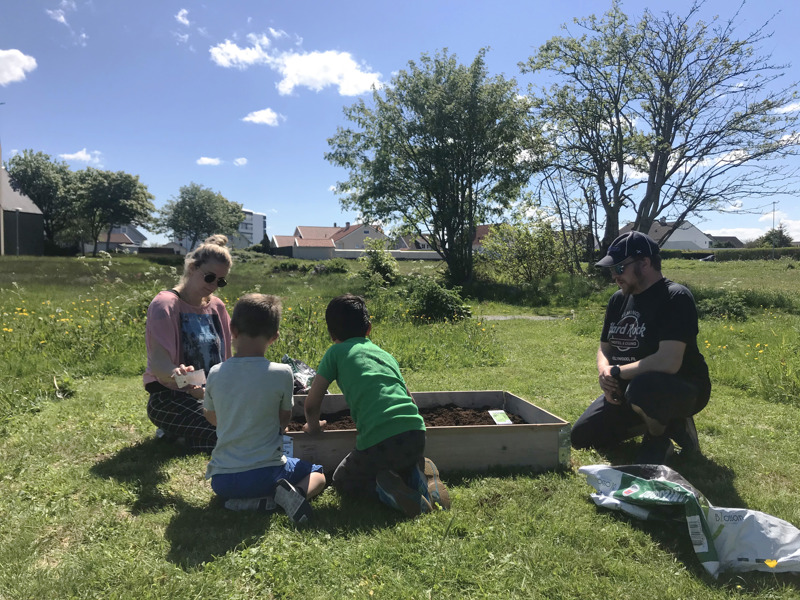 To barn og to voksne rundt en plantekasse i et grøntområde. Foto: Line Møllerop