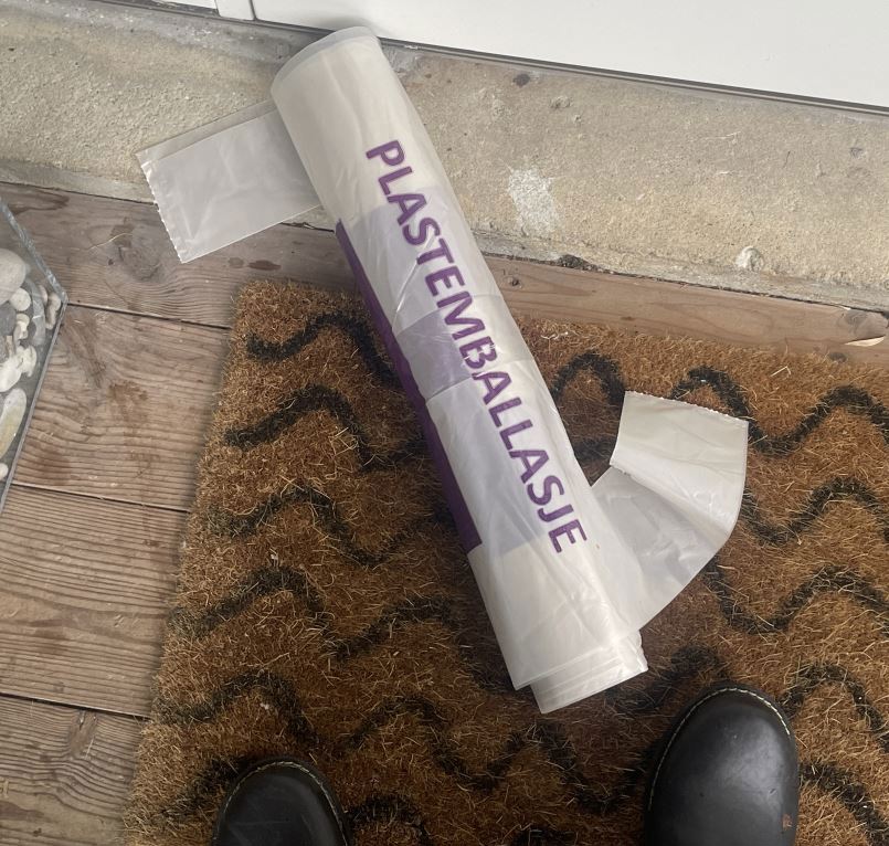Rull med plastsekker merket "Plastemballasje" ligger på ei dørmatte