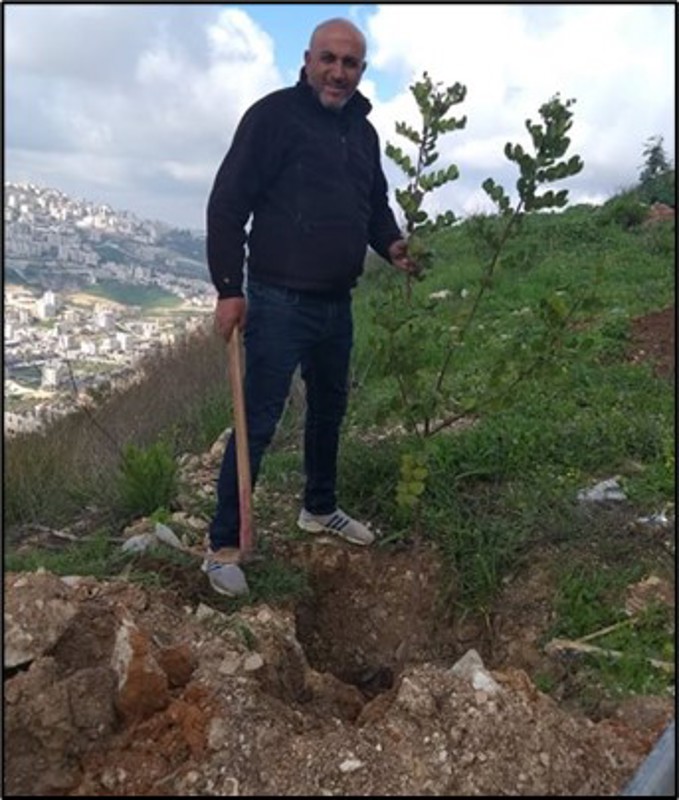 En mann står ved siden av et lite nyplantet tre